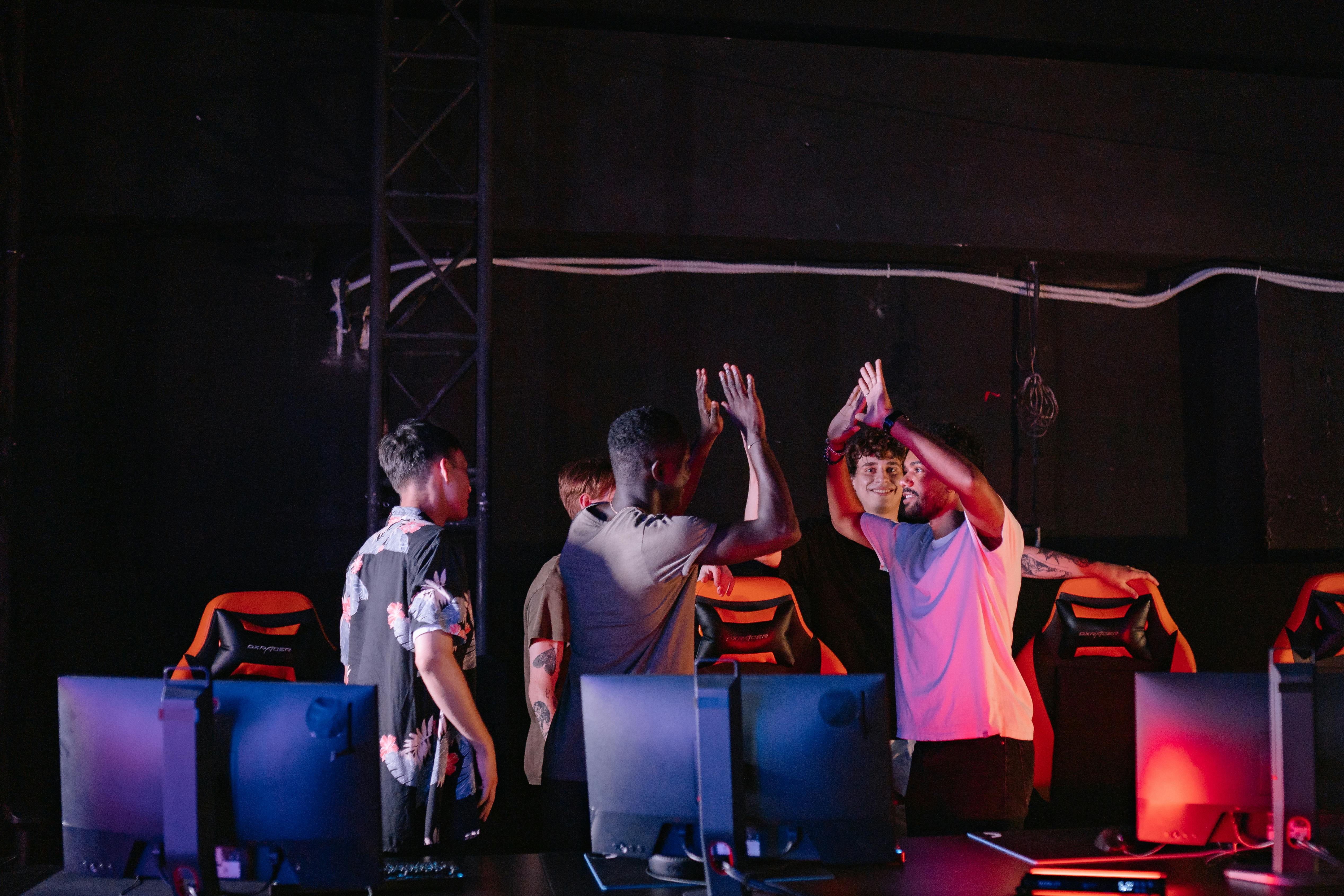 A diverse group of young gamers celebrating a victory with high-fives in a dark gaming room.
