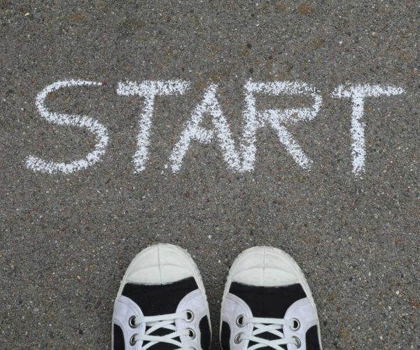 Close-up of sneakers and a 'START' chalk drawing on pavement, symbolizing new beginnings.