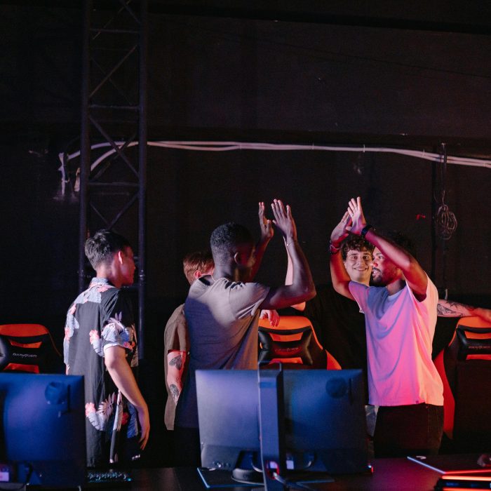 A diverse group of young gamers celebrating a victory with high-fives in a dark gaming room.