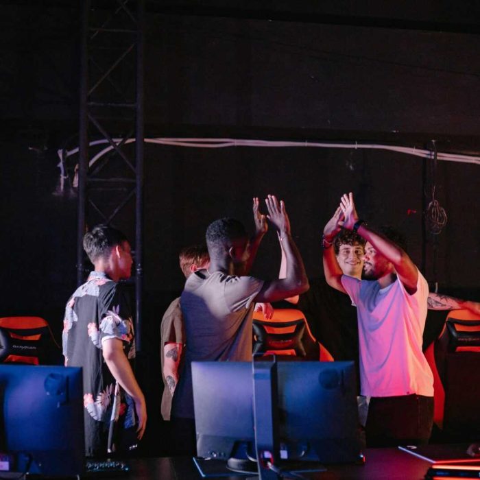 A diverse group of young gamers celebrating a victory with high-fives in a dark gaming room.